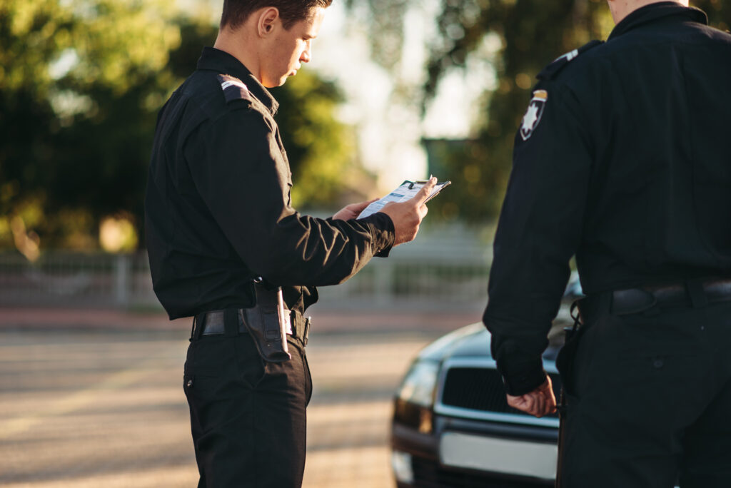 dvaja-policajti-stoja-pri-zastavenom-aute-jeden-vypisuje-dokument-na-podlozke